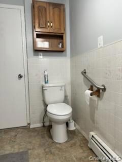 Bathroom with baseboard heating, wainscoting, and tile walls