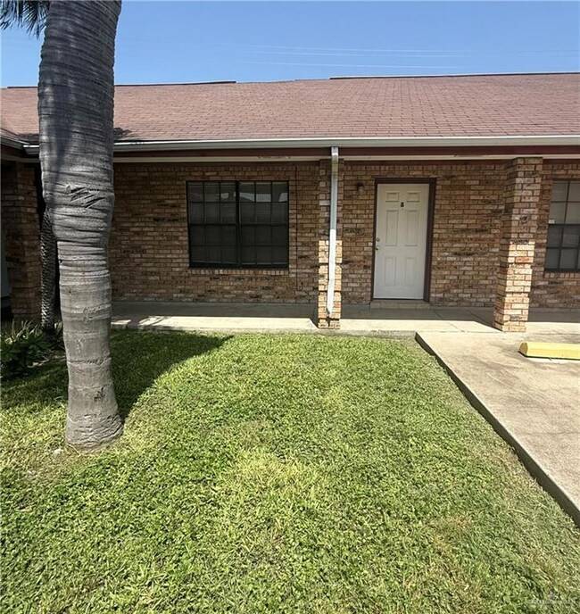 Doorway to property with roof with shingles, brick siding, and a lawn