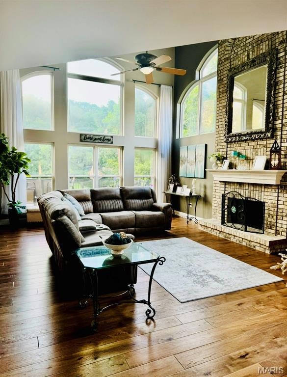 Living room featuring a towering ceiling, a ceiling fan, hardwood / wood-style floors, and a brick fireplace