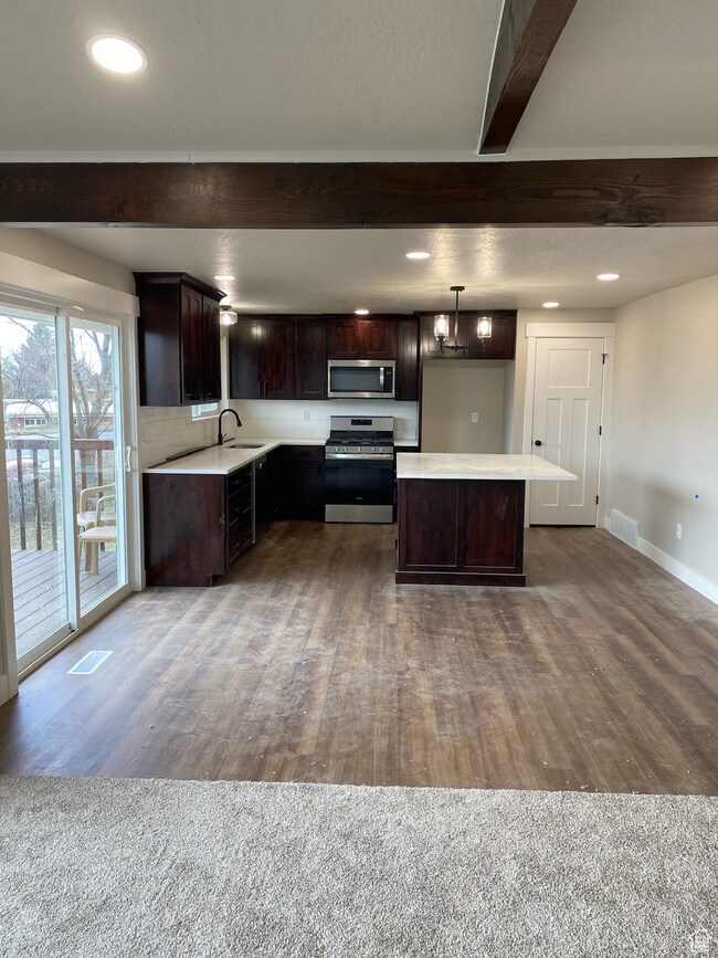 Kitchen featuring beam ceiling, a sink, stainless steel appliances, light countertops, and dark brown cabinets
