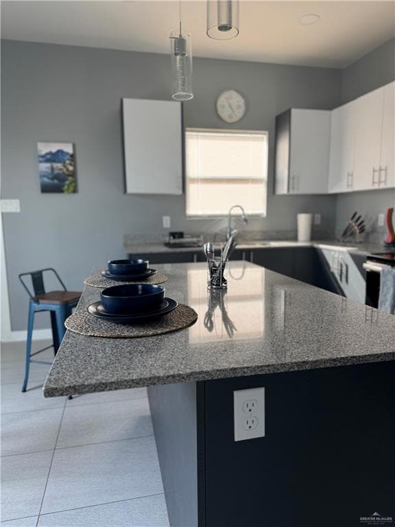 Kitchen with a sink, stone countertops, light tile patterned floors, decorative light fixtures, and white cabinetry