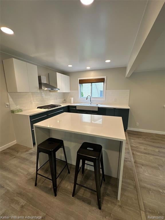 Kitchen with white cabinetry, decorative backsplash, a kitchen bar, a center island, and light wood-type flooring