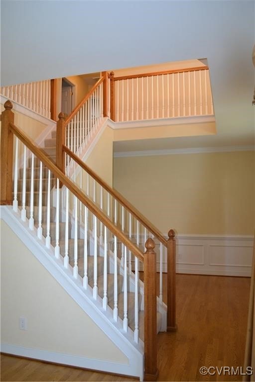 Stairway with crown molding, a wainscoted wall, an