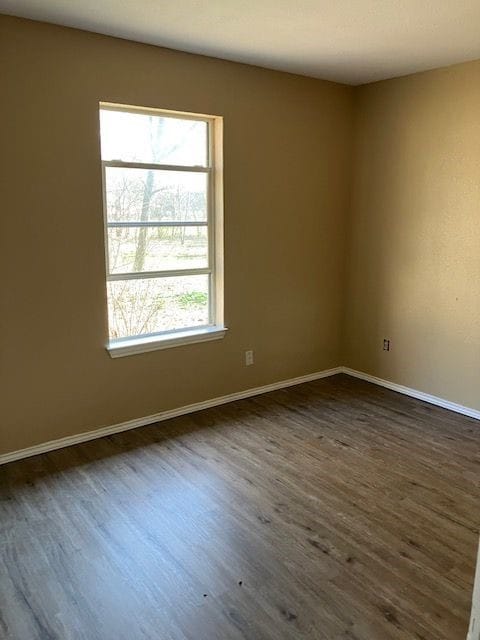 Spare room with dark wood-style flooring and baseboards