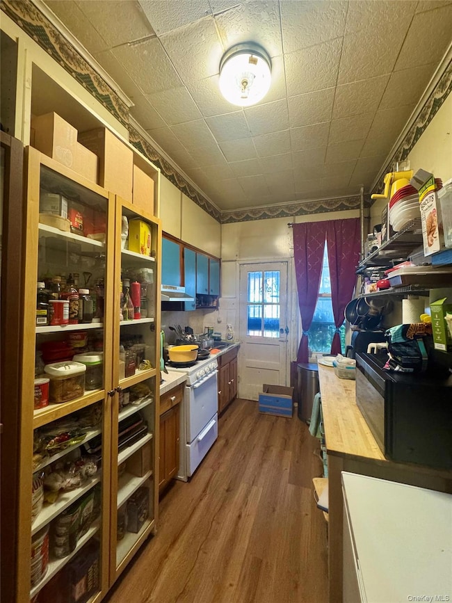 Kitchen with dark wood-type flooring, black microwave, white stove, light countertops, and brown cabinetry