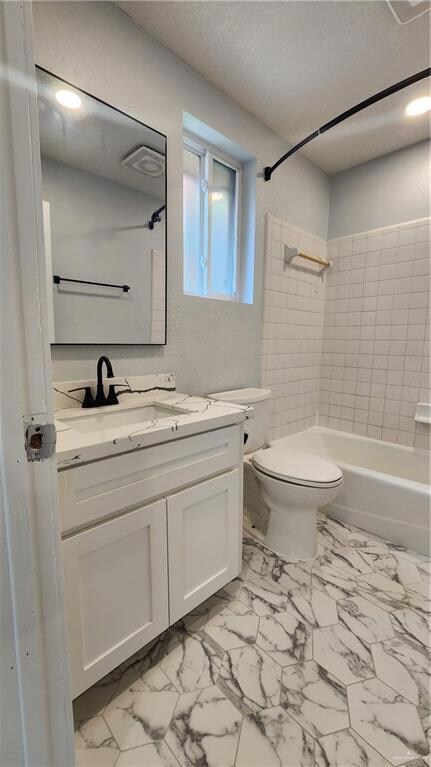 Full bathroom with vanity, toilet, bathtub / shower combination, marble look tiles, and a textured ceiling