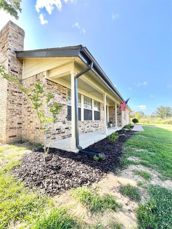 View of side of property featuring brick siding, a chimney, and a yard