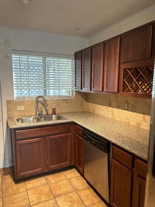 Kitchen featuring a textured ceiling, backsplash, dishwasher, light tile patterned flooring, and light stone counters