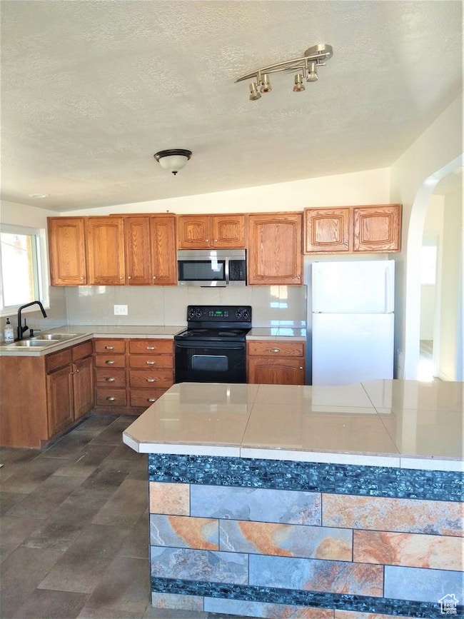 Kitchen featuring arched walkways, black electric range oven, freestanding refrigerator, brown cabinetry, and a textured ceiling