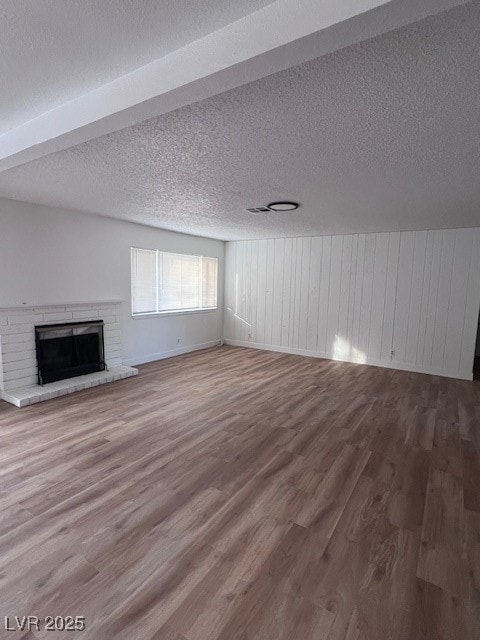 Unfurnished living room featuring a brick fireplace, wood finished floors, a textured ceiling, and wood walls