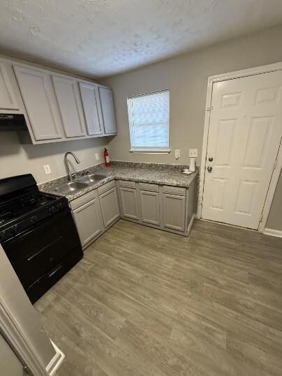 Kitchen featuring a sink, light wood-type flooring, black gas range, and a textured ceiling