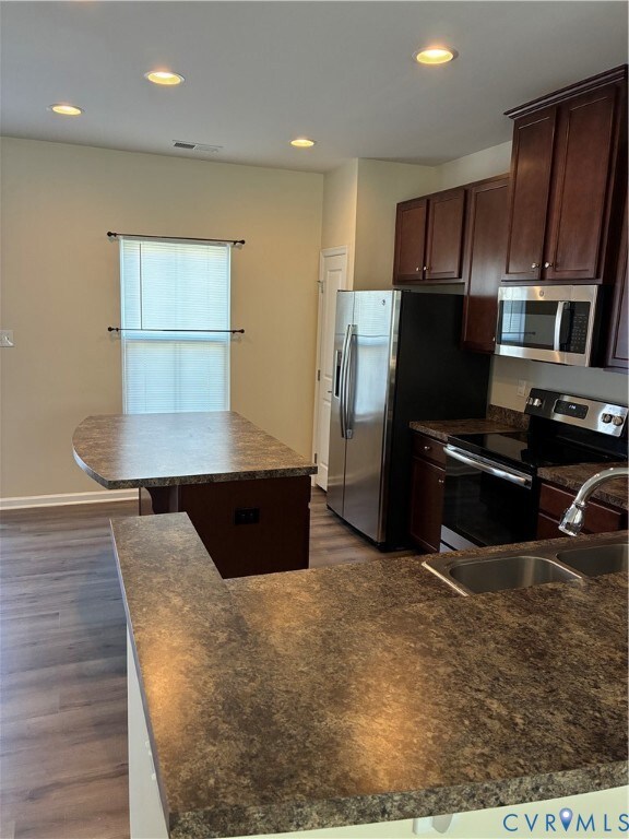 Kitchen featuring dark brown cabinetry, stove, recessed lighting, dark wood finished floors, and a kitchen island