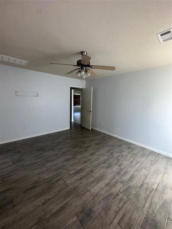 Empty room with ceiling fan, dark wood-type flooring, and baseboards