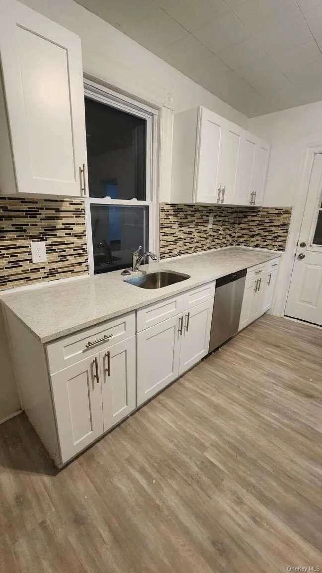 Kitchen featuring white cabinets, dishwasher, light stone countertops, decorative backsplash, and light wood-type flooring