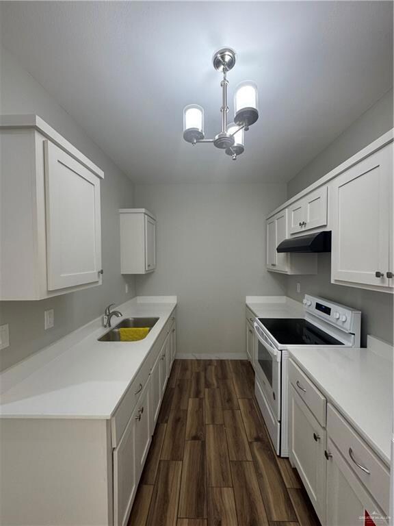 Kitchen with exhaust hood, dark wood-type flooring, range, a sink, and a notable chandelier