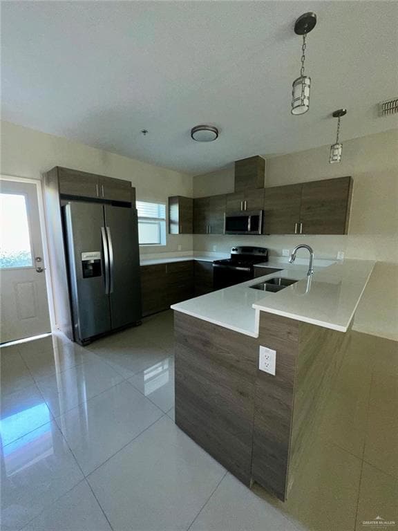 Kitchen featuring modern cabinets, light tile patterned floors, stainless steel appliances, hanging light fixtures, and a peninsula