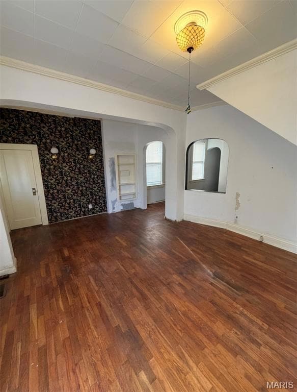 Unfurnished living room with crown molding, arched walkways, and dark wood-type flooring