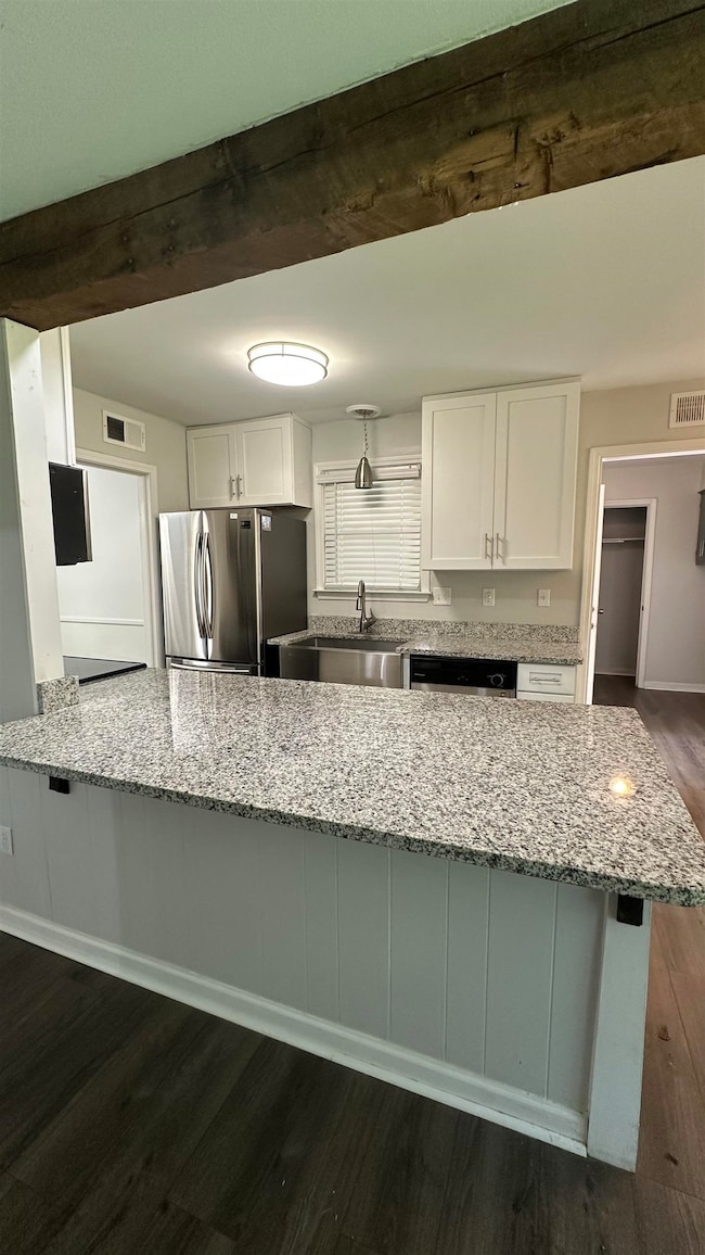 Kitchen featuring appliances with stainless steel finishes, dark wood-style flooring, white cabinetry, light stone countertops, and a peninsula