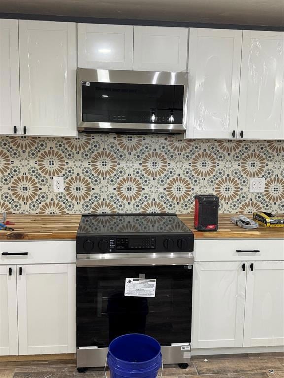 Kitchen featuring stove, white cabinets, tasteful backsplash, and wooden counters