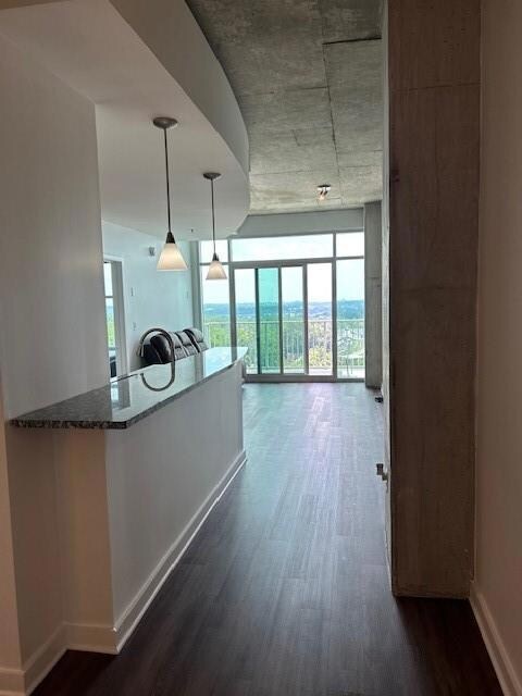 Kitchen featuring dark wood-style floors, pendant lighting, dark stone countertops, and expansive windows