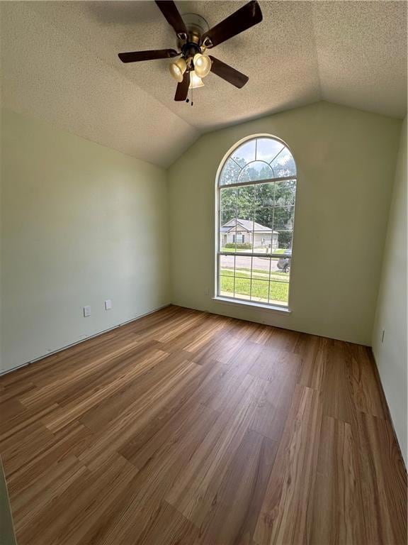 Empty room featuring vaulted ceiling, wood finished floors, ceiling fan, and a textured ceiling