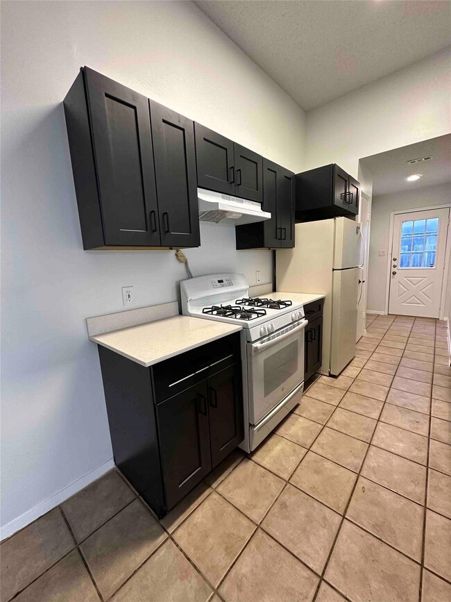 Kitchen with white range with gas cooktop, light countertops, under cabinet range hood, light tile patterned flooring, and dark cabinets