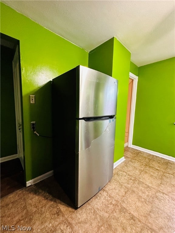 Kitchen with a textured ceiling, stainless steel refrigerator, and light tile floors
