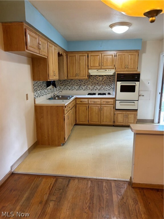 Kitchen with sink, wall oven, light hardwood / wood-style floors, decorative backsplash, and range hood