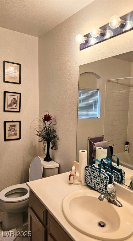 Full bathroom with toilet, a textured wall, vanity