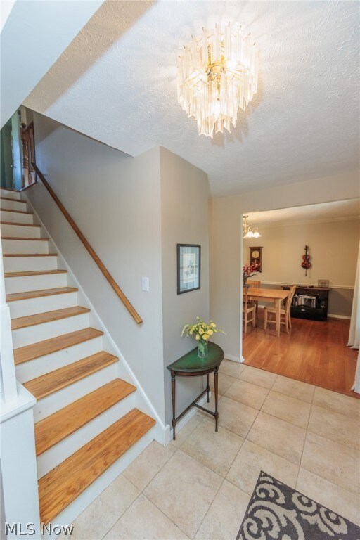 Stairway with a textured ceiling, a chandelier, and light tile flooring