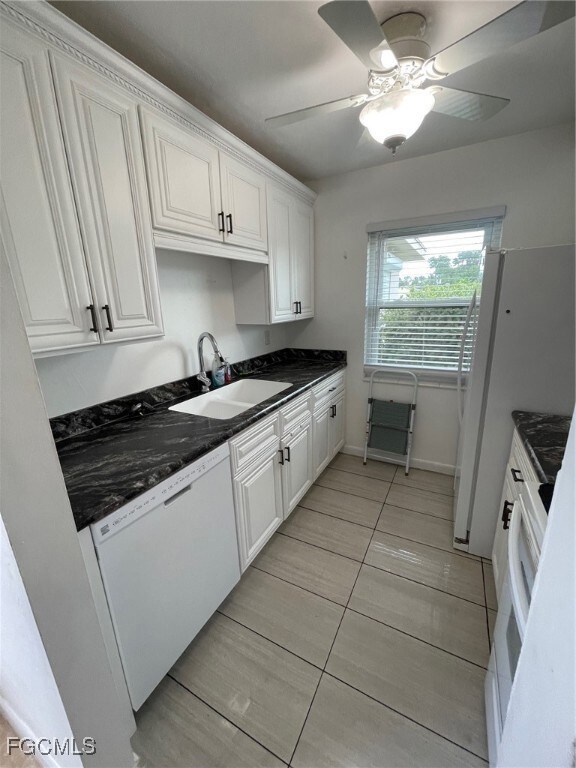 Kitchen with white cabinetry, refrigerator, dishwashing machine, and dark stone countertops