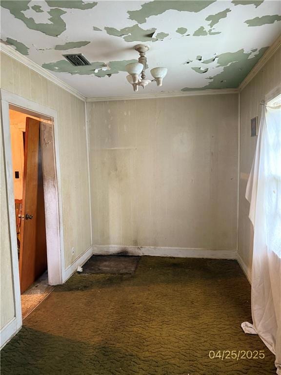 Spare room featuring dark colored carpet, ornamental molding, baseboards, and wooden walls