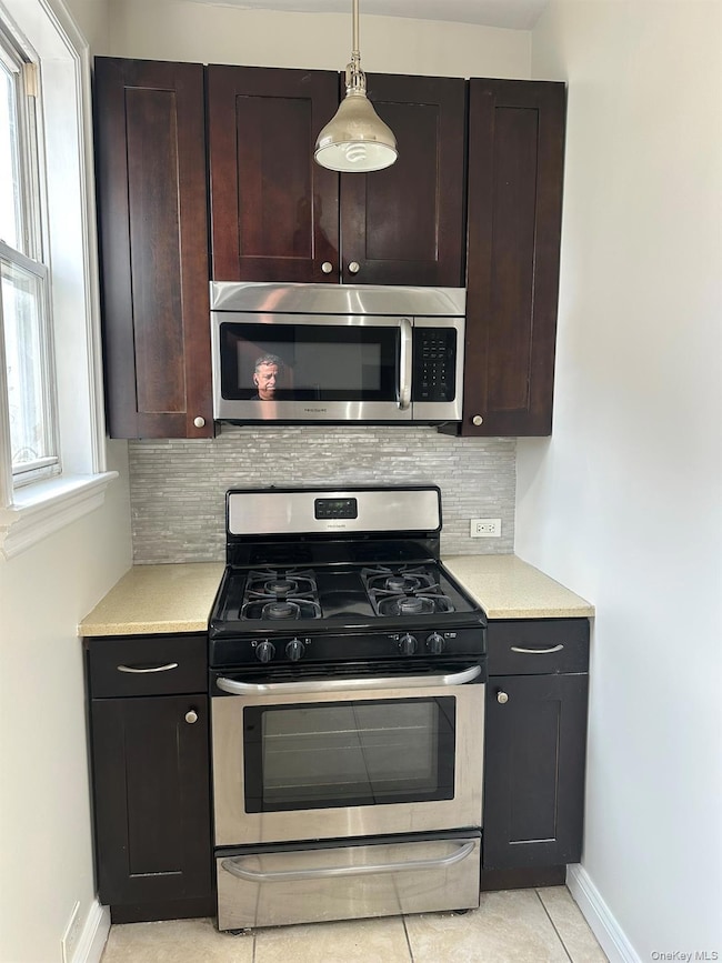 Kitchen featuring appliances with stainless steel finishes, decorative backsplash, hanging light fixtures, light tile patterned floors, and dark brown cabinetry