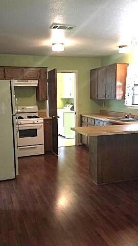 Kitchen featuring light countertops, a textured ceiling, white gas stove, freestanding refrigerator, built in microwave, and dark wood-style floors