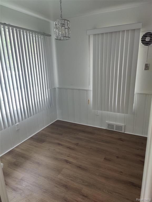 Unfurnished dining area with dark wood-style flooring, a chandelier, and wainscoting