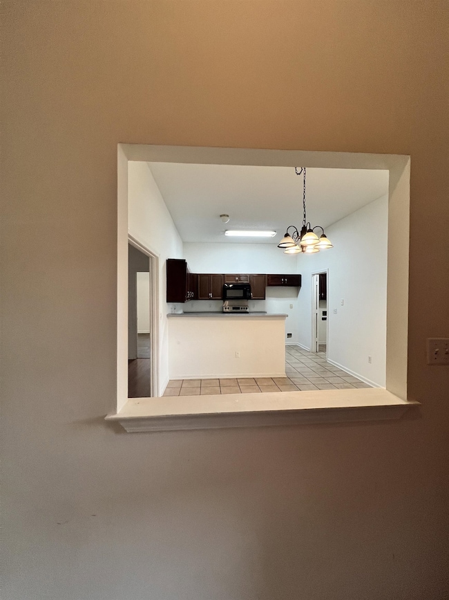 Kitchen featuring dark brown cabinetry, hanging light fixtures, a chandelier, black microwave, and light countertops