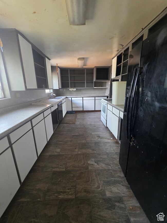 Kitchen with white cabinetry, light countertops, black fridge, and electric range
