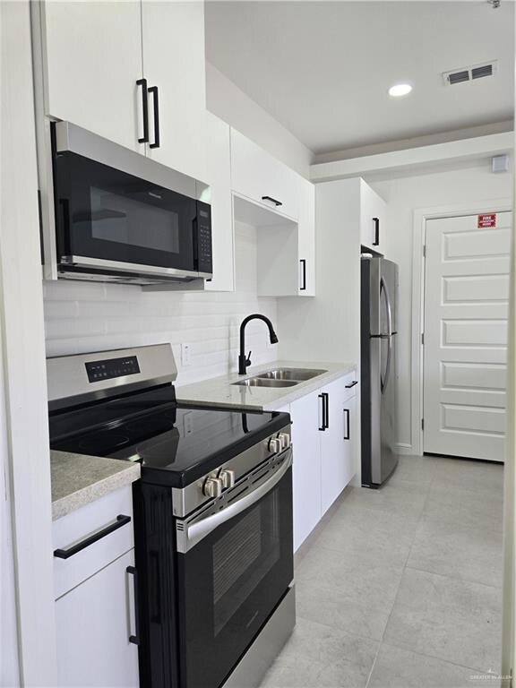 Kitchen featuring stove, a sink, fridge, white cabinets, and recessed lighting