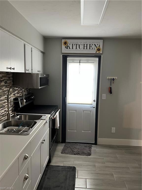 Kitchen with stove, a sink, decorative backsplash, and white cabinetry