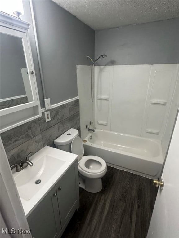 Full bath with dark wood finished floors, vanity, a textured ceiling, bathing tub / shower combination, and tile walls