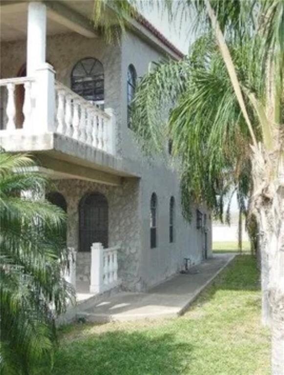 Back of property with a balcony, a porch, stucco siding, and a yard
