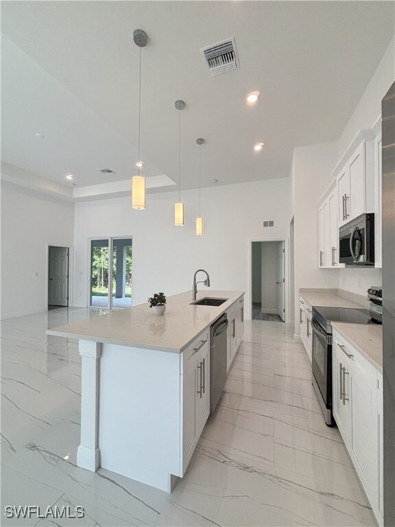 Kitchen with appliances with stainless steel finishes, light marble finish floors, a sink, a large island with sink, and recessed lighting