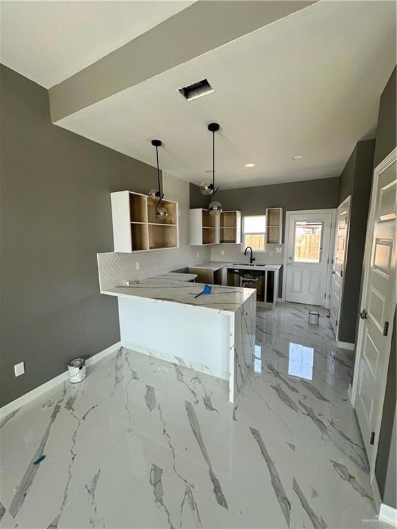 Kitchen featuring kitchen peninsula, tasteful backsplash, sink, light tile floors, and pendant lighting