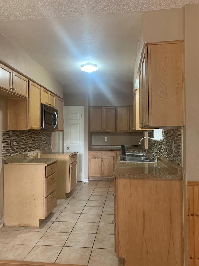 Kitchen with decorative backsplash, stainless steel microwave, and light tile patterned flooring