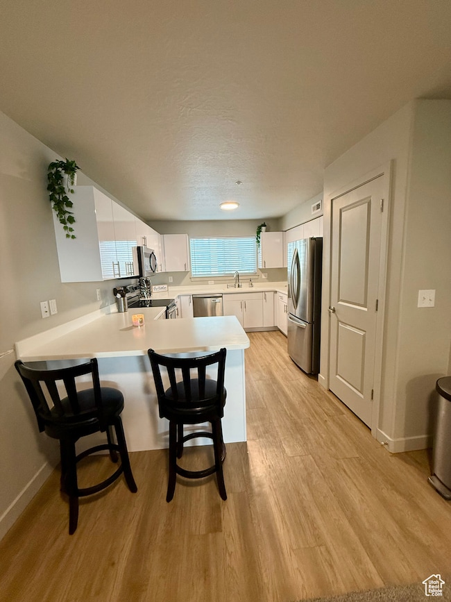 Kitchen featuring white cabinets, light countertops, a kitchen bar, and light wood finished floors