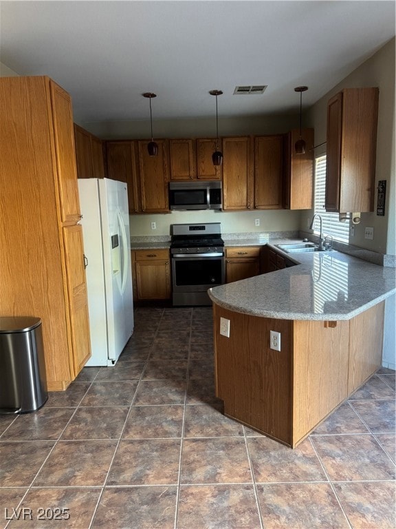 Kitchen with appliances with stainless steel finishes, decorative light fixtures, a peninsula, brown cabinetry, and light stone counters