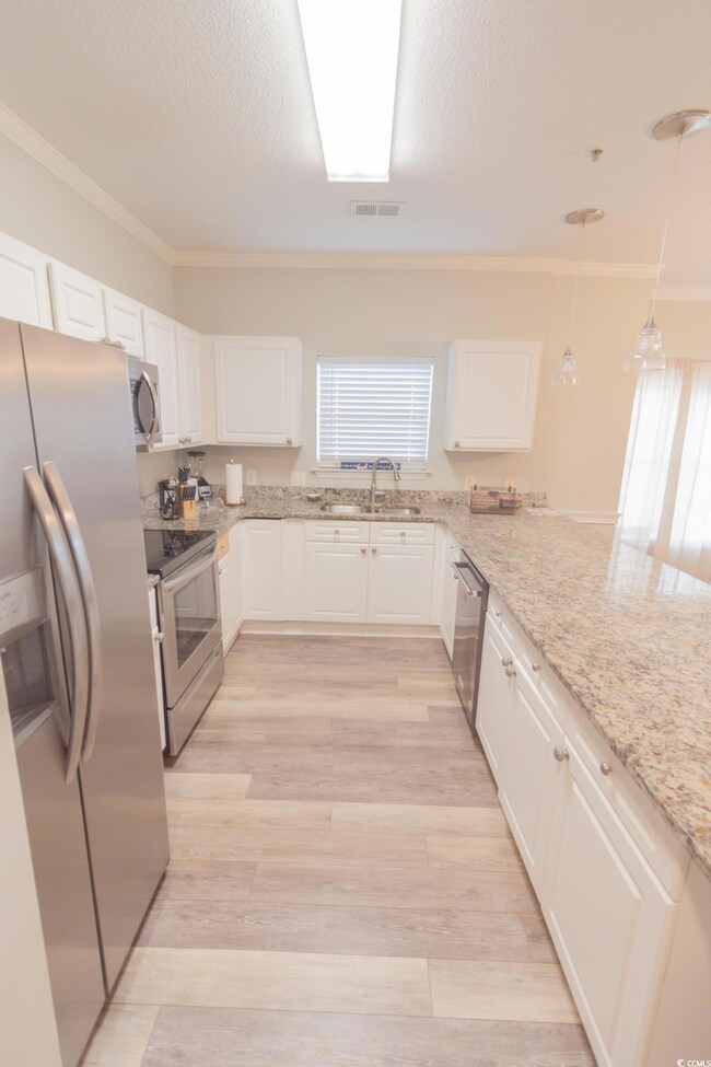 Kitchen with ornamental molding, stainless steel appliances, white cabinetry, light wood finished floors, and light stone counters