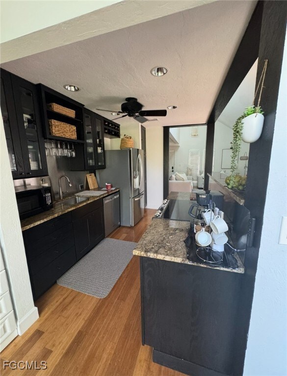 Kitchen featuring dark cabinets, light wood-style flooring, glass insert cabinets, a textured ceiling, and appliances with stainless steel finishes
