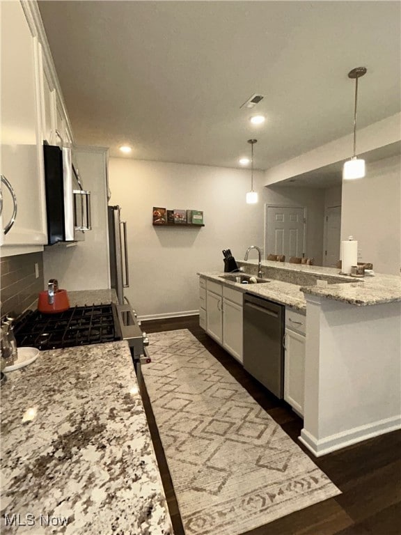 Kitchen featuring white cabinetry, light stone countertops, pendant lighting, dark wood-style floors, and appliances with stainless steel finishes