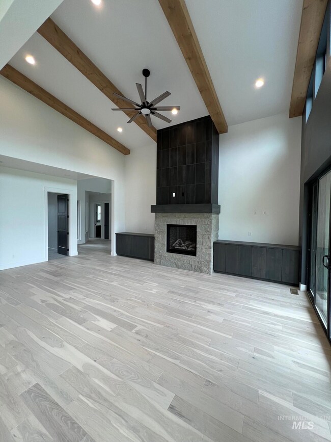 Unfurnished living room featuring beamed ceiling, a large fireplace, ceiling fan, light wood finished floors, and recessed lighting